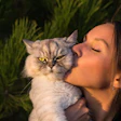Soft-furred gray cat receiving a gentle kiss near green foliage