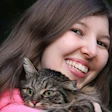 Smiling young woman hugging a tabby cat with green eyes