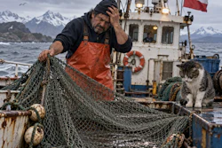 Fisherman on Chilean vessel mending nets with snowy mountains and cat nearby