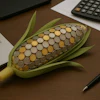 Corn-shaped container filled with coins on wooden desk beside laptop and calculator