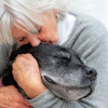 Senior woman with white hair tenderly kissing an older black dog in a warm, affectionate moment