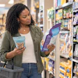 Woman comparing food packages in grocery store aisle while holding shopping basket