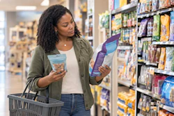 Woman comparing food packages in grocery store aisle while holding shopping basket